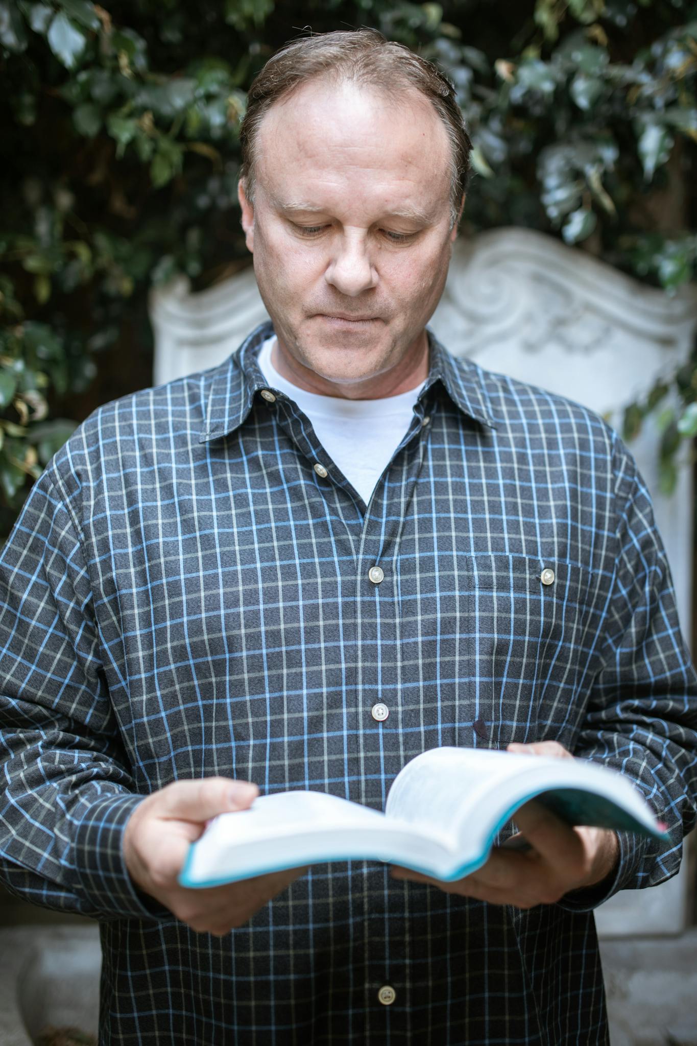 An adult man reads a Bible outdoors, exuding peace and contemplation in a serene setting.
