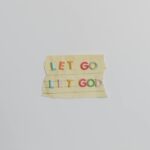 Minimalist image of a torn paper with the phrase 'Let Go, Let God' in colorful letters.