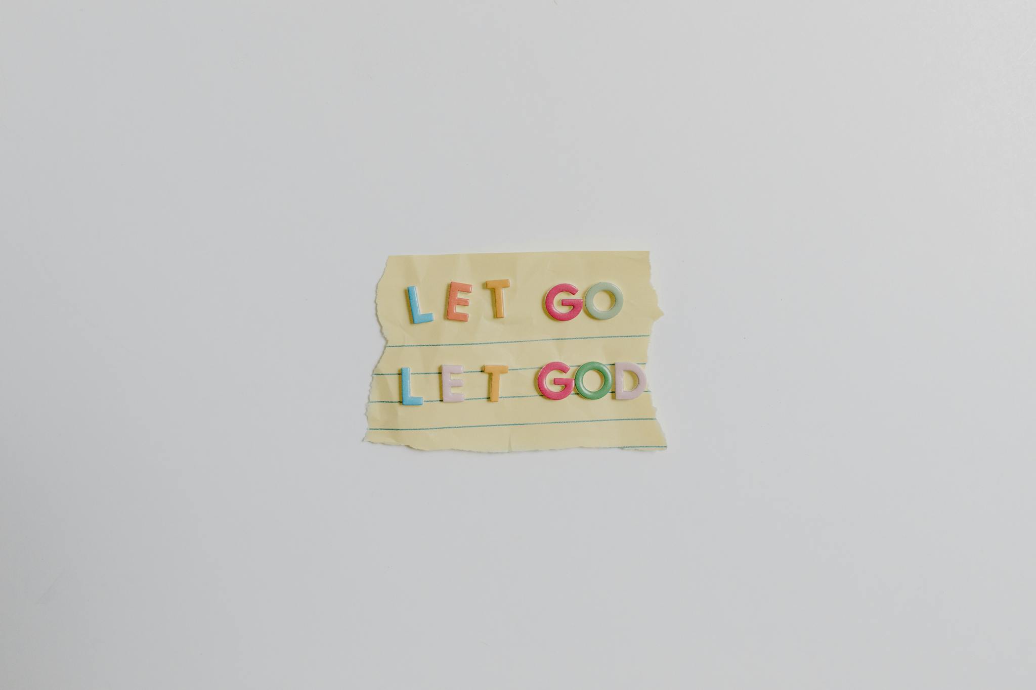 Minimalist image of a torn paper with the phrase 'Let Go, Let God' in colorful letters.