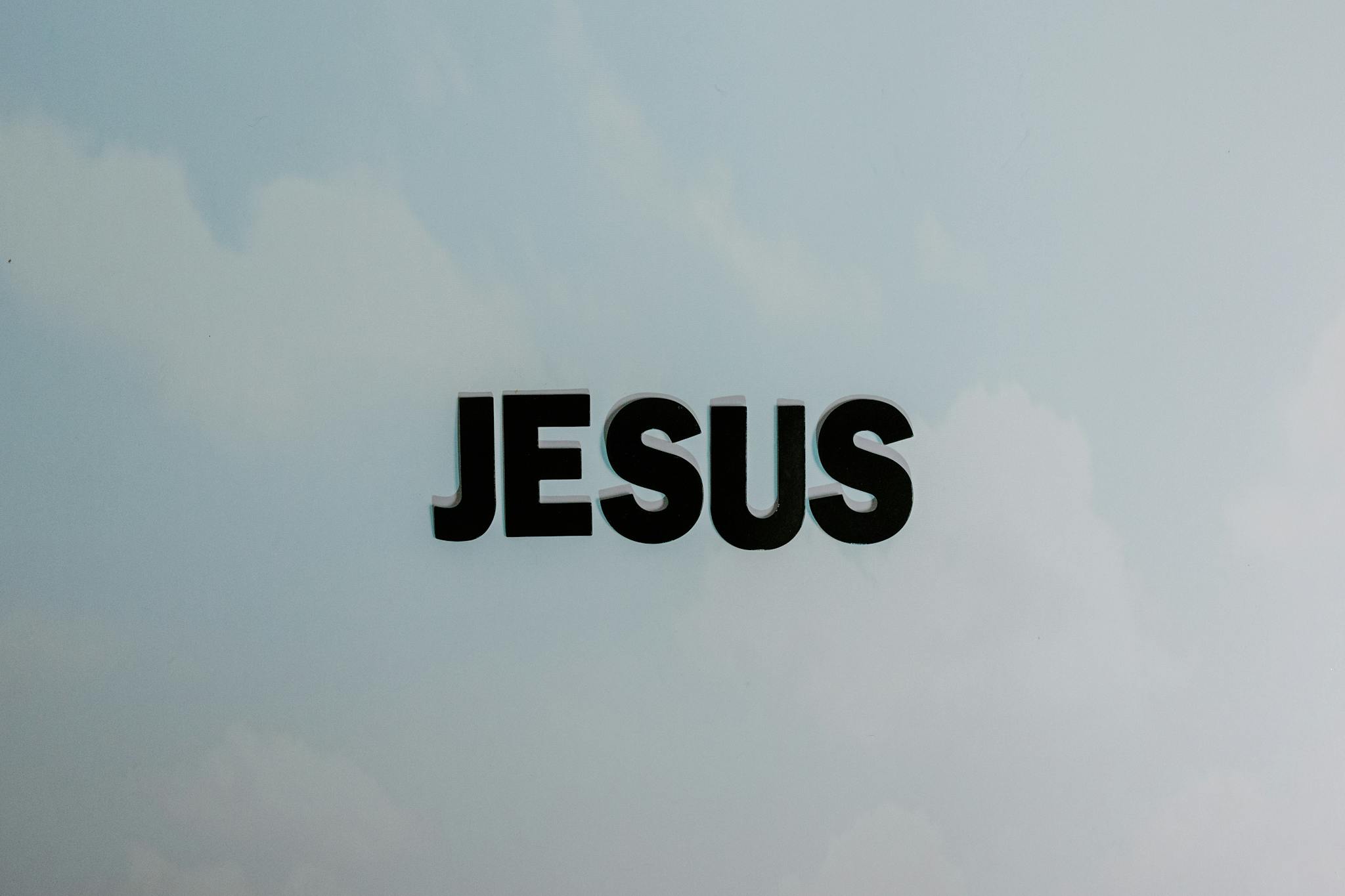 Minimalist image with bold 'JESUS' text against a cloudy sky background.